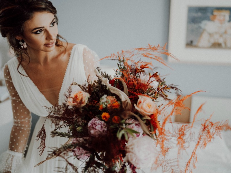 In questa foto una ragazza tiene in mano il suo bouquet da sposa scomposto nei toni dell'arancione, del rosa e del bordeaux