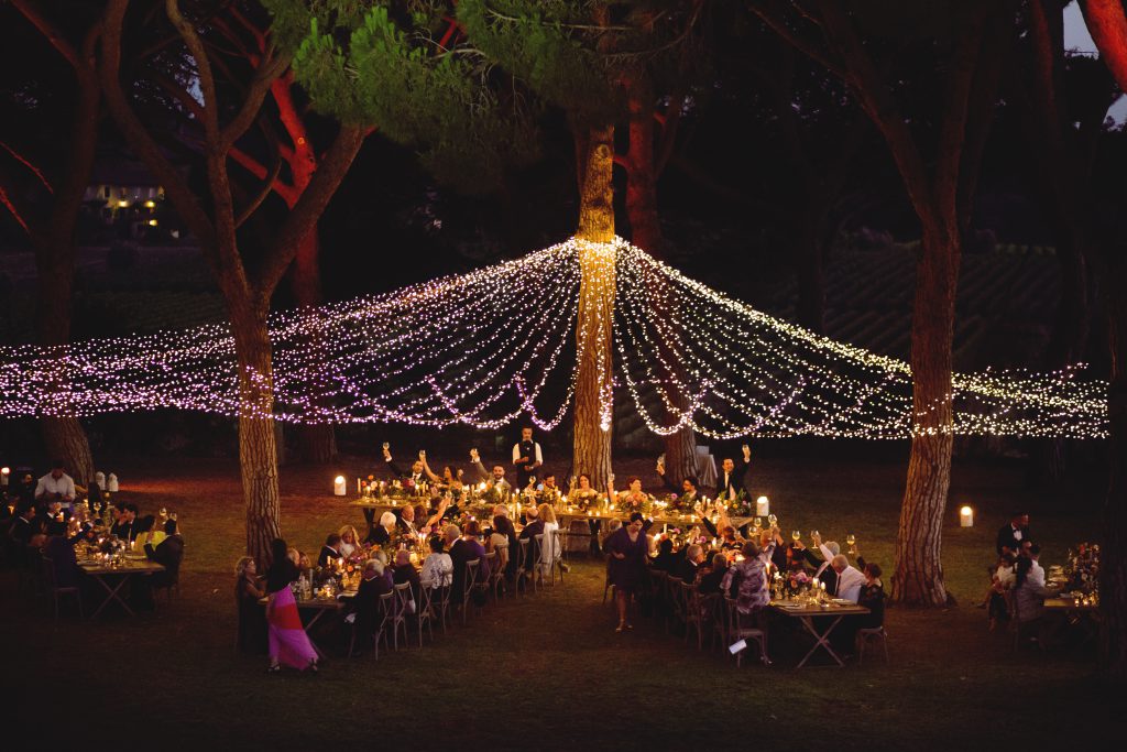 In quesa foto i fili di luci tra gli alberi creano un tetto illuminato sui tavoli del banchetto nuziale all'aperto