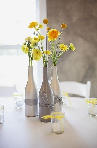In questa foto tre bottiglie a collo lungo e in grigio ospitano fiori di campo gialli