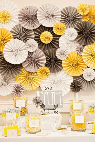 In questa foto fiori di carta maxi tingono di giallo grigio e bianco la parte dietro alla confettata del matrimonio