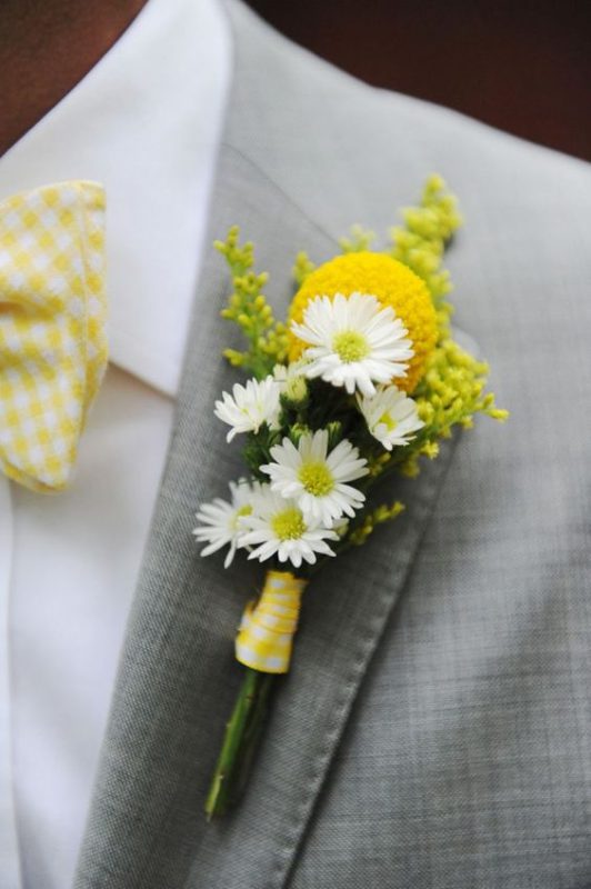 In questa foto un fiore all'occhiello giallo per uno sposo con vestito grigio e papillon giallo