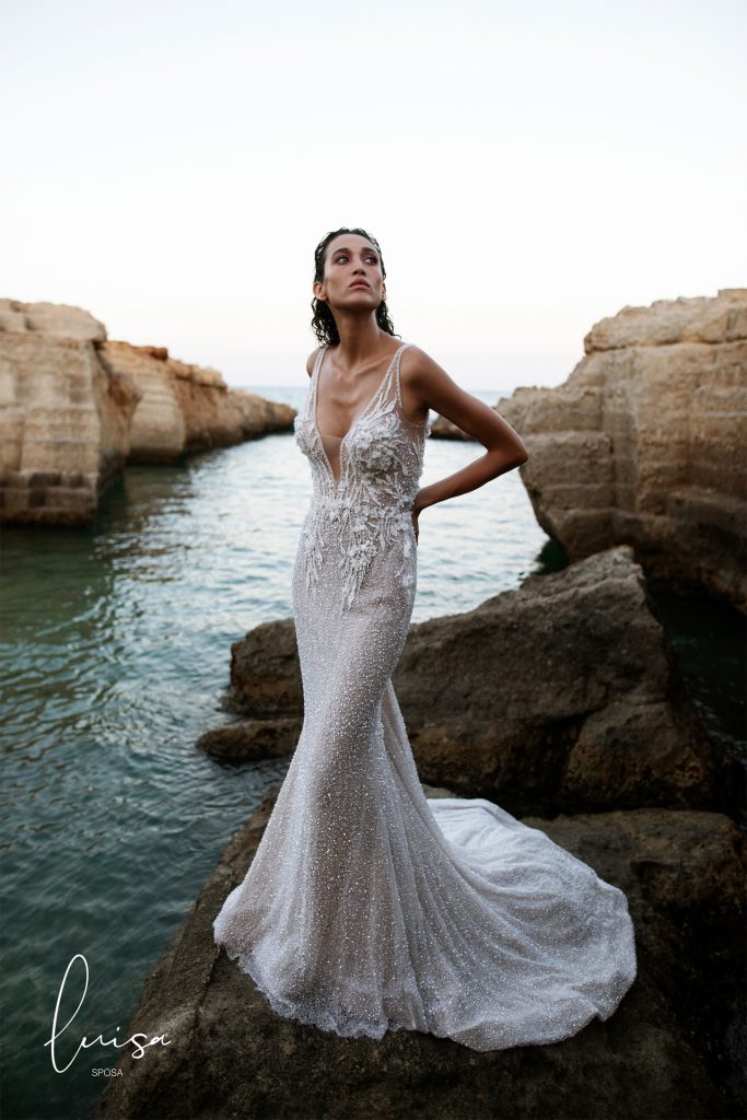 In questa foto una modella in posa vicino al mare con addosso un abito da sposa a sirena della collezione Luisa Sposa 2021