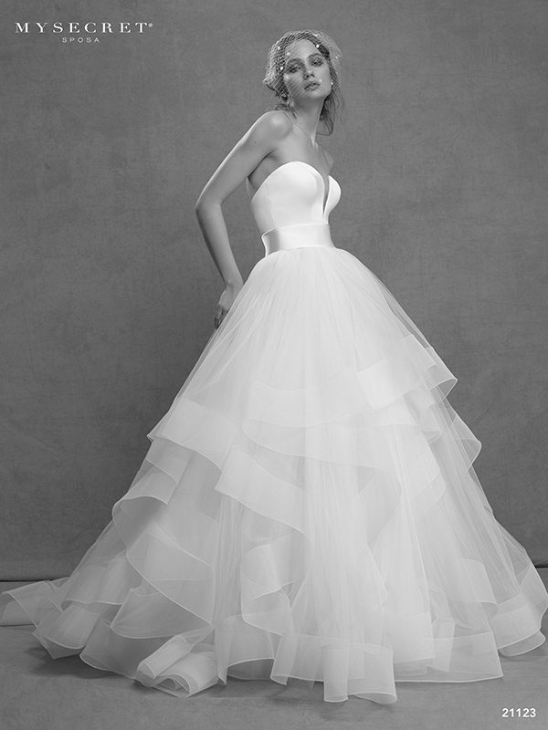 In questa foto una modella indossa un vaporoso abito a balze in tulle della collezione My Secret Sposa 2021