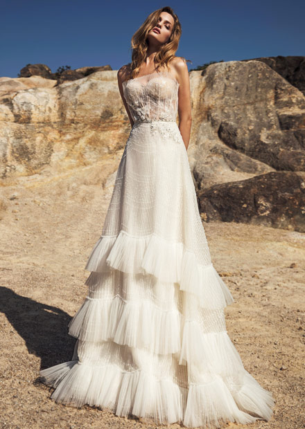 In questa foto una modella indossa un abito da sposa con balze e punti luce perfetto per un matrimonio bordo piscina