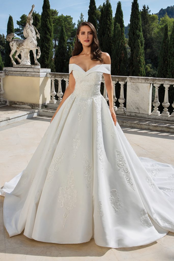 In questa foto una modella indossa un abito da sposa con scollatura off-shoulder di Justin Alexander