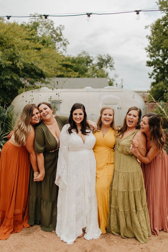 In questa foto una sposa con le damigelle: le ragazze indossano abiti di modelli e colori diversi, nei toni autunnali del verde, ocra, porpora