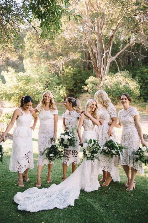 In questa foto una sposa vestita di bianco insieme alle sue damigelle di matrimonio anche loro con vestiti bianchi ma longuette 