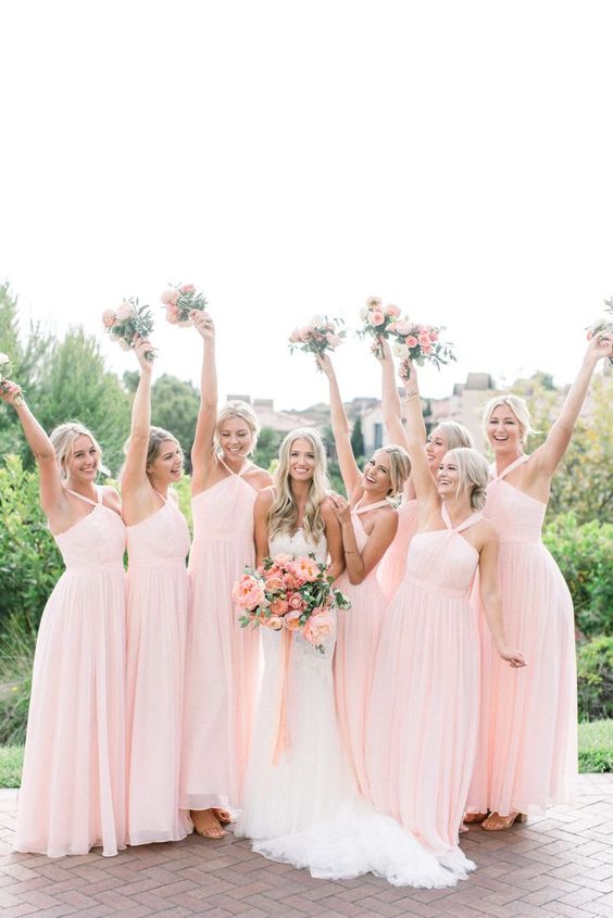 In questa foto una sposa e le sue damigelle vestite con abiti rosa confetto, tutti dello stesso modello. Tra le mani hanno bouquet con fiori della stessa tonalità di rosa