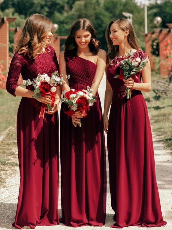 In questa foto tre damigelle indossano abiti lunghi colore bordeaux con bouquet di fiori in coordinato