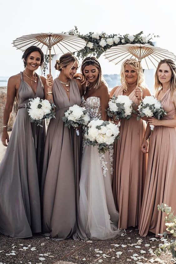 In quesa foto una sposa con le sue damigelle vestite nei toni che sfumano dal rosa al lavanda. Tengono tra le mani i bouquet e gli ombrellini di carta per ripararsi dal sole