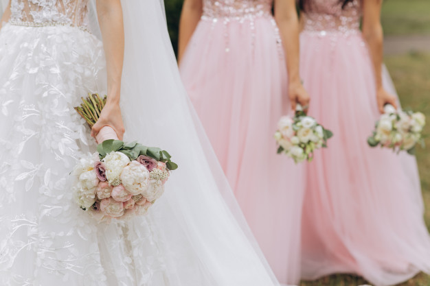 In questa foto una sposa seguita dalle sue damigelle del matrimonio vestite di rosa. Tutte e tre le ragazze hanno in mano il loro bouquet di fiori