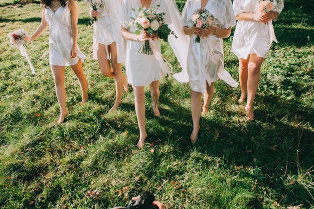 In questa foto una sposa insieme alle sue tre damigelle in sottoveste, mentre passeggiano su un prato verde scalze