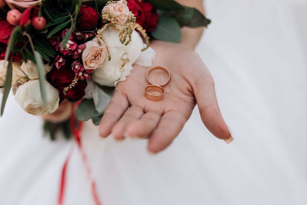 In questa foto due fedi nuziali nella mano di una donna, che con l'altra tiene anche un bouquet da sposa