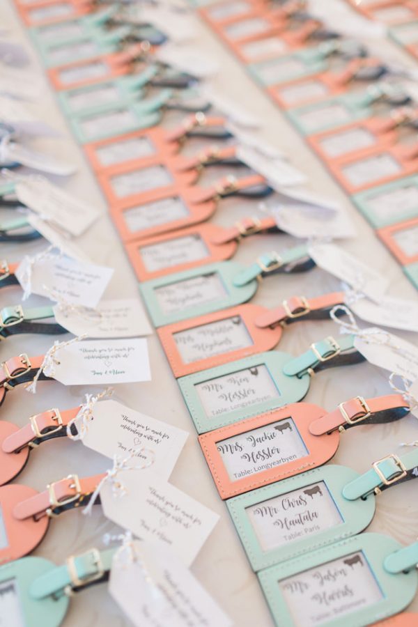 In questa foto delle escort card per un matrimonio a tema viaggio realizzate con targhette per valigie nei colori del pesca e del Tiffany
