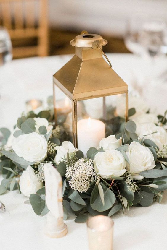 In questa foto un centrotavola per un matrimonio con lanterna di colore ore, rose e peonie bianche, alloro e candele