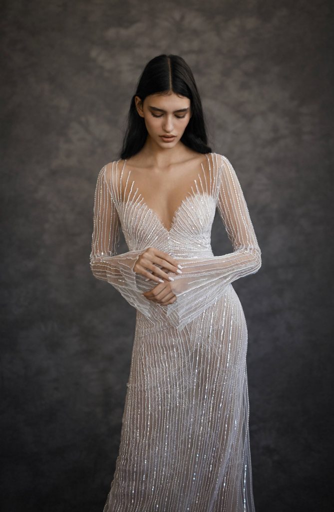 In questa foto una modella fotografata per tre quarti mentre indossa un abito da sposa Dana Harel 2022 presentato alla New York Bridal Fashion Week 2021 