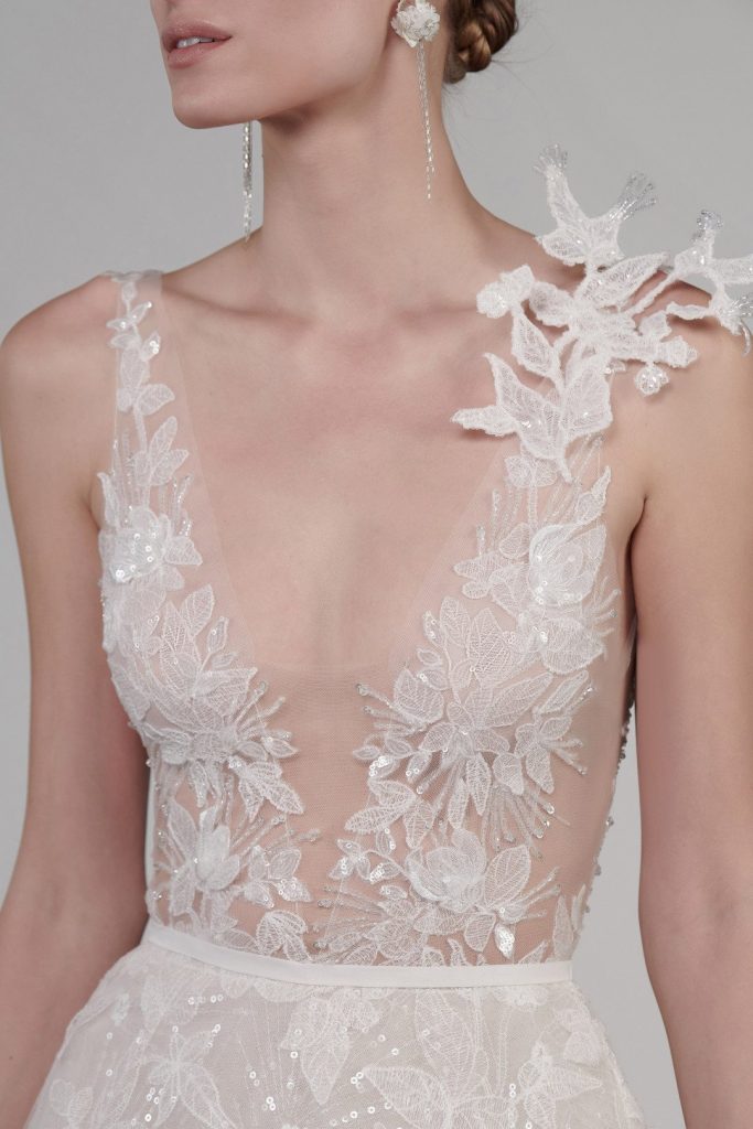 In questa foto il dettaglio del top di un abito da sposa Mira Zwillinger 2022: la scollatura è profonda e a V, sulla spalla un ramage floreale in pizzo 3D