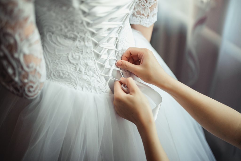 In questa foto il dettaglio posteriore del corpetto di un abito da sposa mentre una donna lo stringe in vita