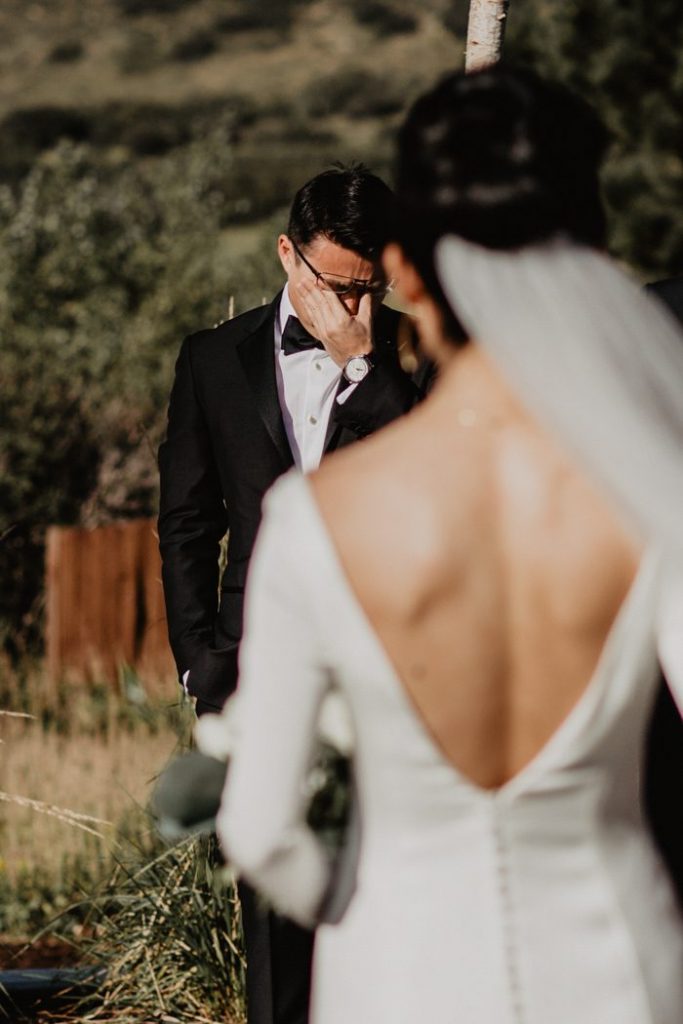 In questa foto lo sposo si commuove dopo aver visto la sua sposa, ritratta di spalle e fuori fuoco, per la prima volta in abito bianco 