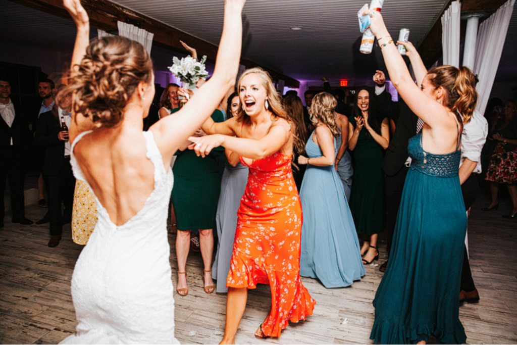 In questa foto la sposa balla con le sua amiche durante il party di nozze. La sposa è ripresa di spalle mentre alza le braccia e guarda un'amica che la indica ridendo