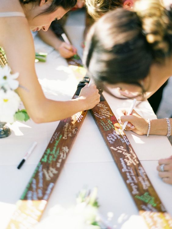 In questa foto alcuni ospiti di un matrimonio firmano un guestbook realizzato con due sci, perfetto per un matrimonio in montagna