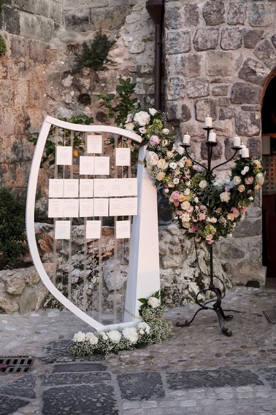 In questa foto un arpa in legno viene usata come tableau mariage a tema musica. Le card con le liste degli invitati divisi per tavolo sono appese alle corde. Completano la decorazione un grande candelabro in bronzo e allestimenti floreali in rosa e bianco