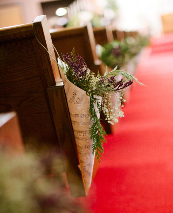 In questa foto coni realizzati con spartiti musicali e contenenti fiori di campo decorano i banchi di una chiesa allestita per un matrimonio a tema musica