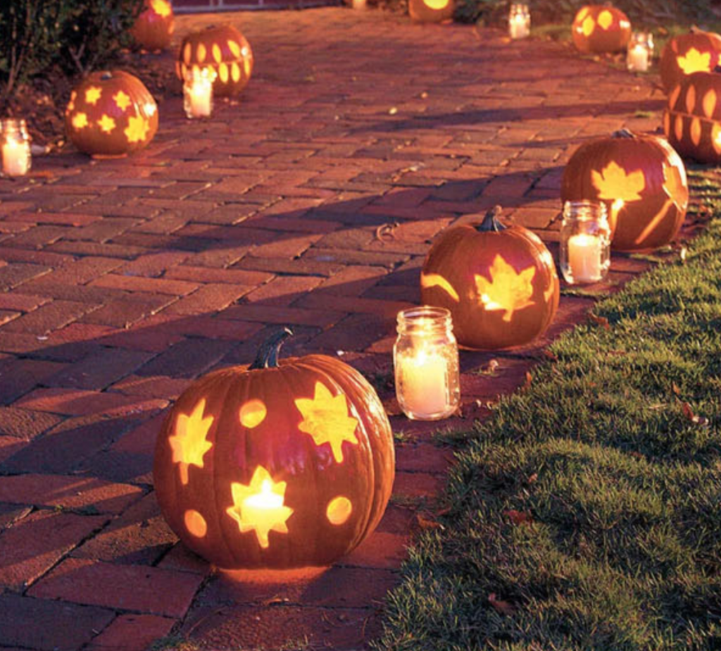 In questa foto un vialetto decorato con lanterne di zucche e vasette con candele bianche, decorazioni perfette per un matrimonio a tema Halloween