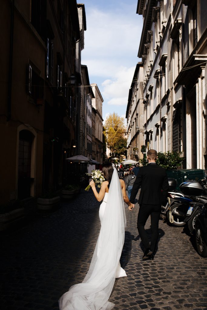 In questa foto una coppia di sposi ripresa di spalle, mentre cammina per le strade di Roma