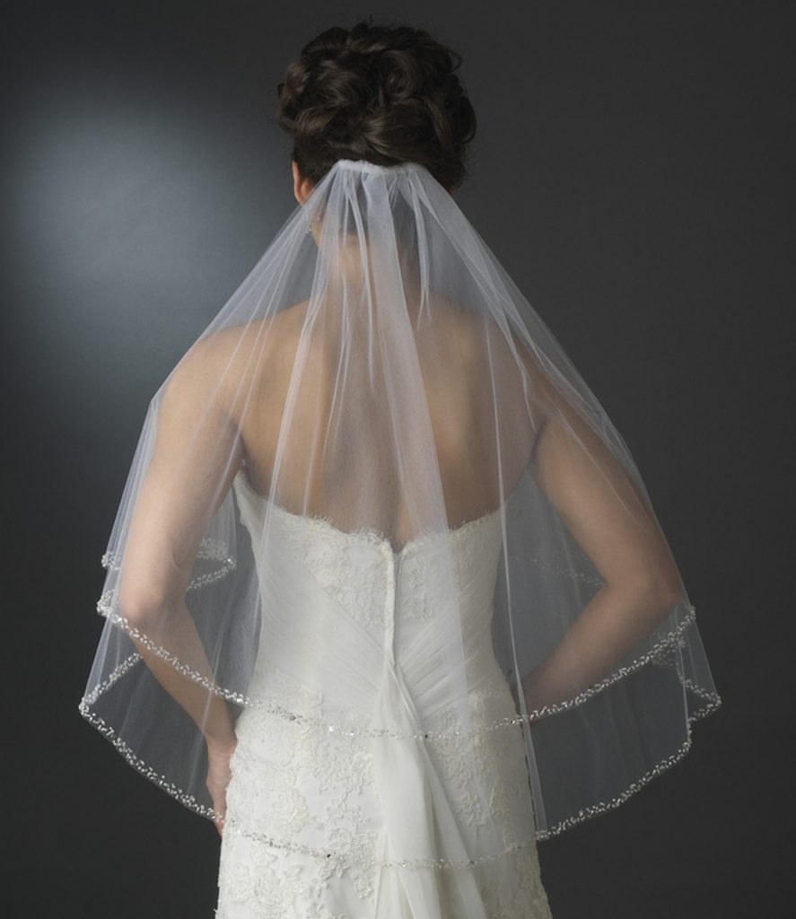 In questa foto una modella indossa un  velo da sposa a gomito su due lunghezze con bordo di perline fissato sotto uno chignon