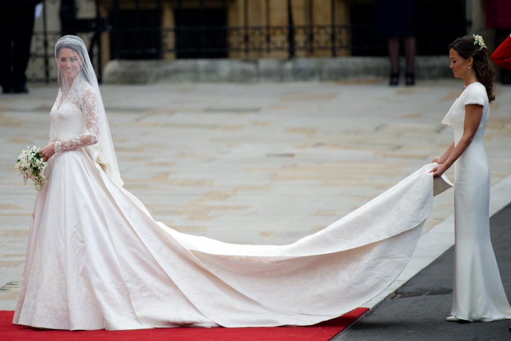 In questa foto Kate Middleton nel giorno del suo matrimonio prima di entrare nell'Abbazia di Westminster. Indossa un abito in taffetà con lungo strascico retto dalla sorella Pippa Middleton e maniche in pizzo con scollatura Queen Anne. Kate ha abbinato un velo ai fianchi in tulle con calata sotto il quale si intravede la tiara