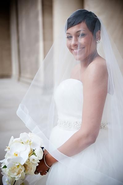 In questa foto una sposa indossa un velo alla vita con bordo largo in tulle e calata abbinato ad un abito con scollo a cuore. Porta tra le mani un bouquet di rose bianche e orchidee