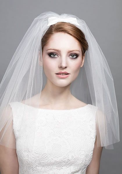 In questa foto una sposa con capelli corti indossa un velo da sposa con fiocchetto sulla testa, a viso scoperto e che le copre solo le spalle 