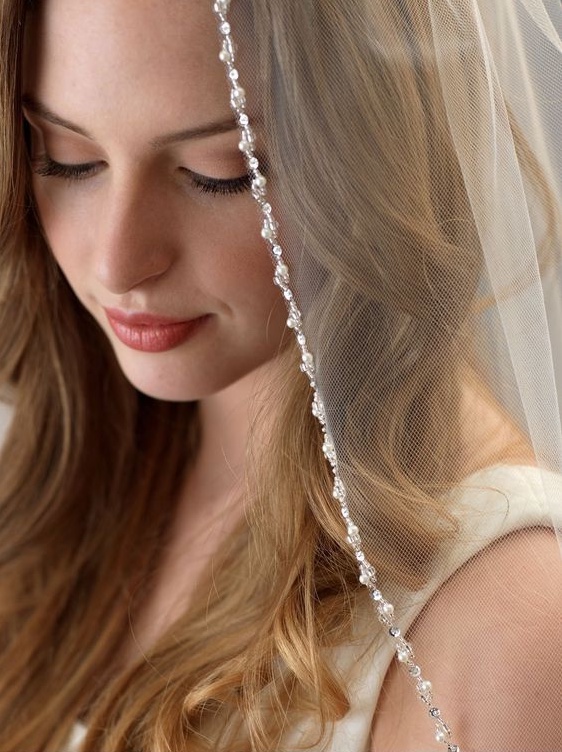 In questa foto una modella posa con un velo da sposa con i bordi di cristalli