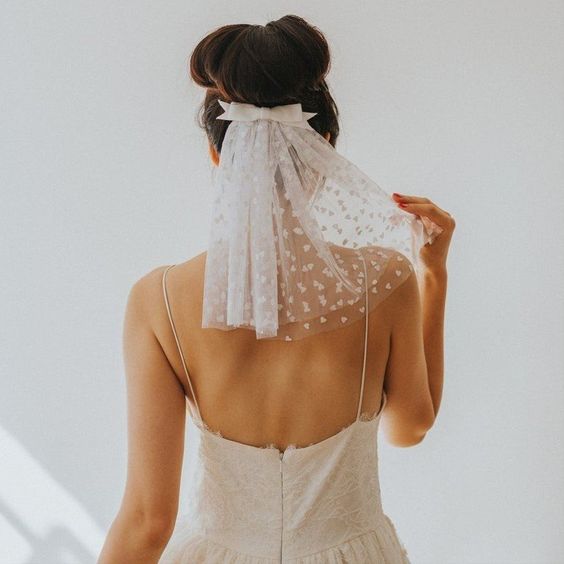 In questa foto una sposa ritratta di spalle indossa un velo corto con cuoricini fermato sotto lo chignon da un fiocco