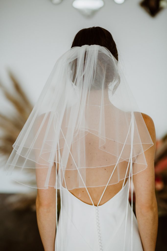 In questa foto una sposa indossa una velo Flyaway in tulle con bordino ricamato 