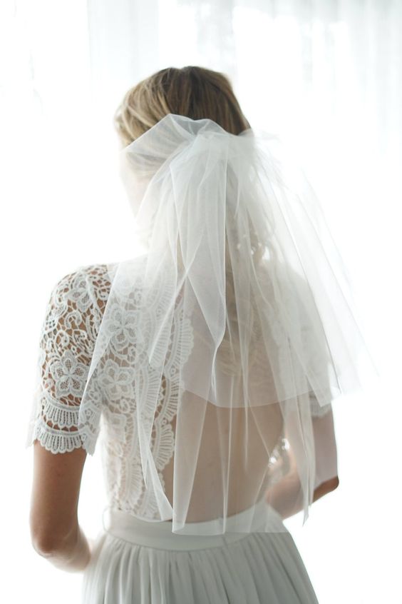 In questa foto una sposa con un velo a scialle in tulle con calata portata indietro e fermato a metà della nuca. La sposa indossa un abito in pizzo macramè scollato sulle spalle