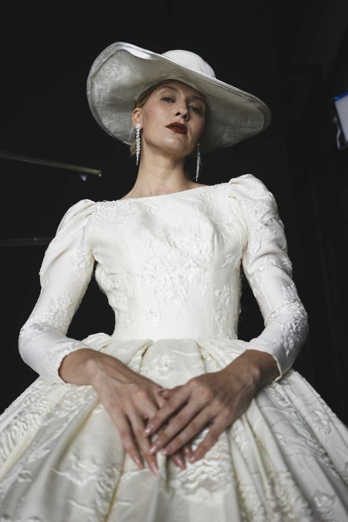 In questa foto un modello della collezione sposa 2022 di Amelia Casablanca con cappello e ricami in pizzo