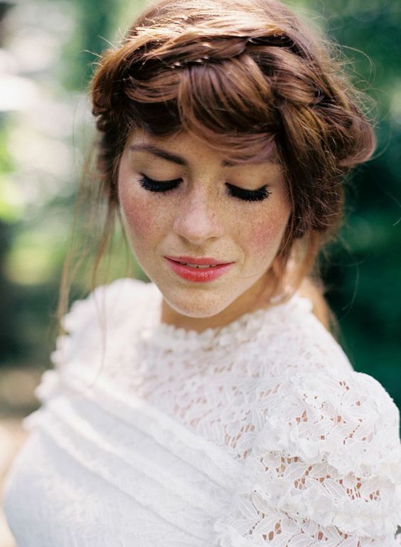 In questa foto una sposa con lentiggini posa ad occhi chiusi. Indossa un abito in pizzo San Gallo e un'acconciatura raccolta con trecce 