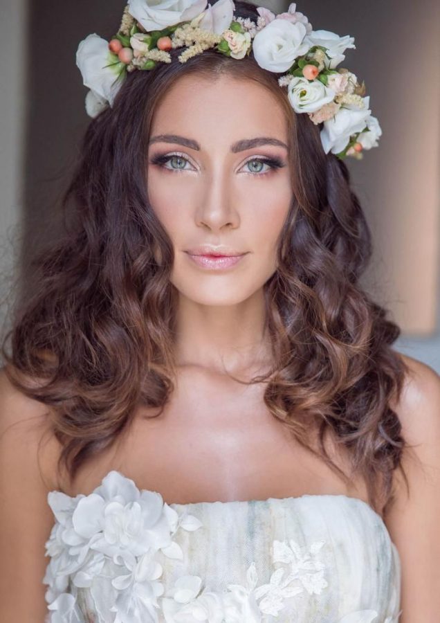 In questa foto una modella con capelli mossi indossa una corona di fiori bianchi e bacche rosa. È truccata con ombretti dai toni perlati e un gloss rosato