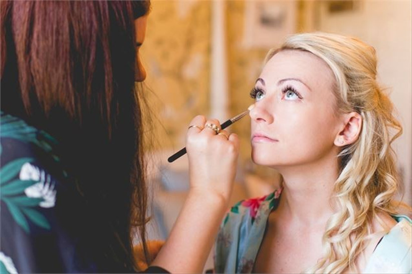 In questa foto una make up artist ripresa di spalle mentre trucca una sposa che guarda verso l'alto