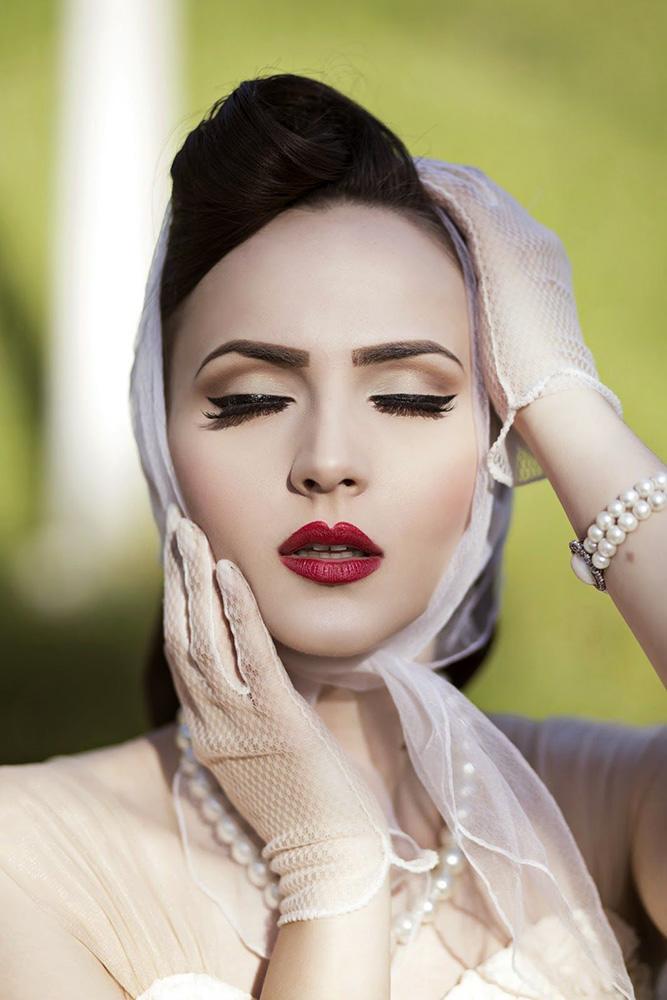 In questa foto un trucco da sposa ispirato agli anni 50 con sopracciglia ben delineate, riga di eyeliner effetto vinile e rossetto rosso intenso. Il viso ha un incarnato matte effetto porcellana. Sulle guance è presente un leggero velo di blush. La modella indossa un foulard e guanti corti bianchi 