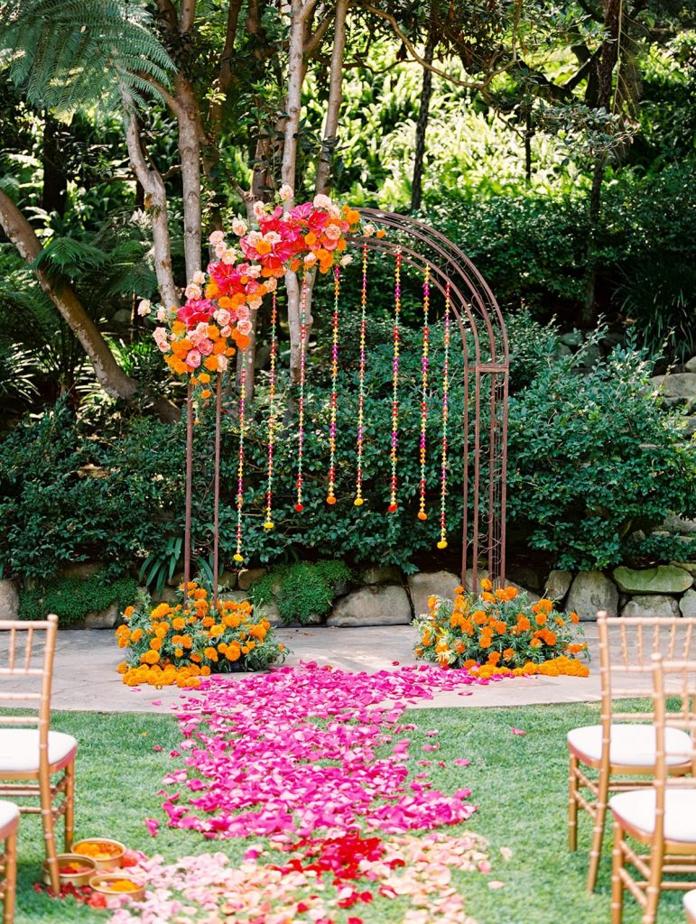 In questa foto l'allestimento di un matrimonio civile in giardino con fiori fuxia e arancioni. Al centro è presente un arco metallico con fiori pendenti come catenelle