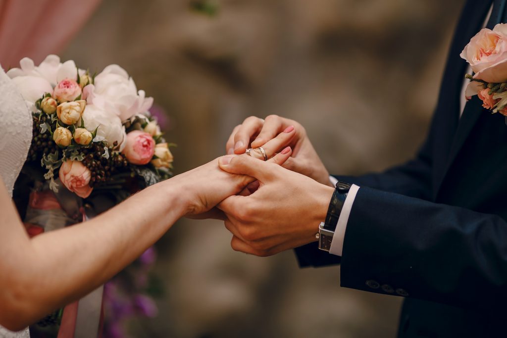 In questa foto vengono riprese solo mani degli sposi. Lo sposo mette la fede al dito della sposa. Si intravede anche il bouquet 