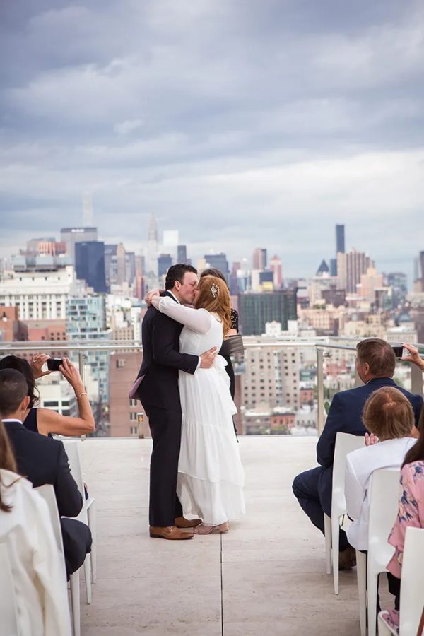 In questa foto due sposi si baciano alla fine del loro matrimonio civile sui tetti di New York. Sullo sfondo si intravede la città