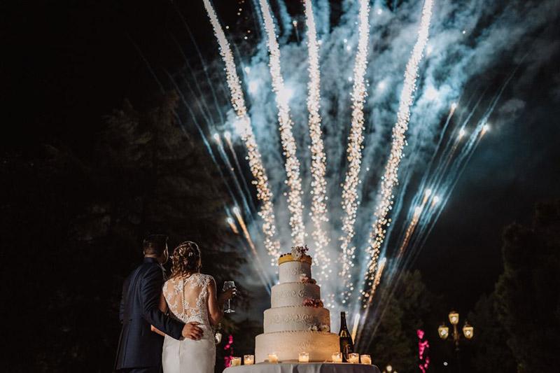 Una coppia di sposi e i fuochi d'artificio durante il taglio della torta