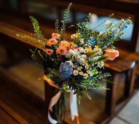 In questa il dettaglio di una decorazione per una chiesa matrimonio realizzata con fiori di campo nei colori del rosa, azzurro e bianco con piccole margherite e foglie di felce