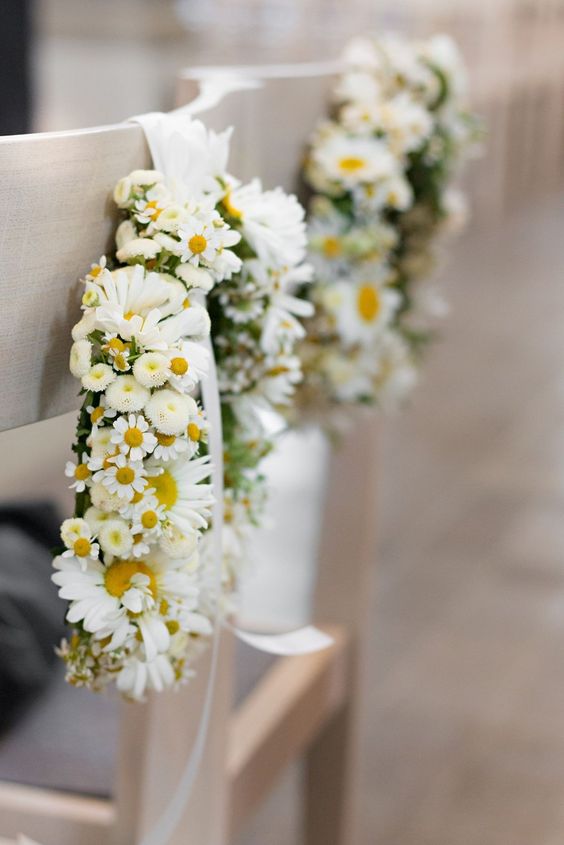 In questa foto due composizioni di margherite piccole e grandi a forma circolare appese con un nastro di raso bianco a due sedie bianche per un matrimonio 