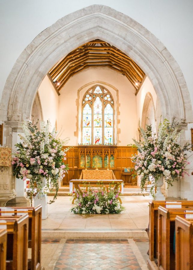 In questa foto l'altare di una chiesa per matrimonio con archi di marmo decorato con composizioni in vasi bianchi con fiori rosa e bianchi sistemate ai lati. In basso, davanti al tavolo della mensa, è adagiata un'altra composizione abbinata