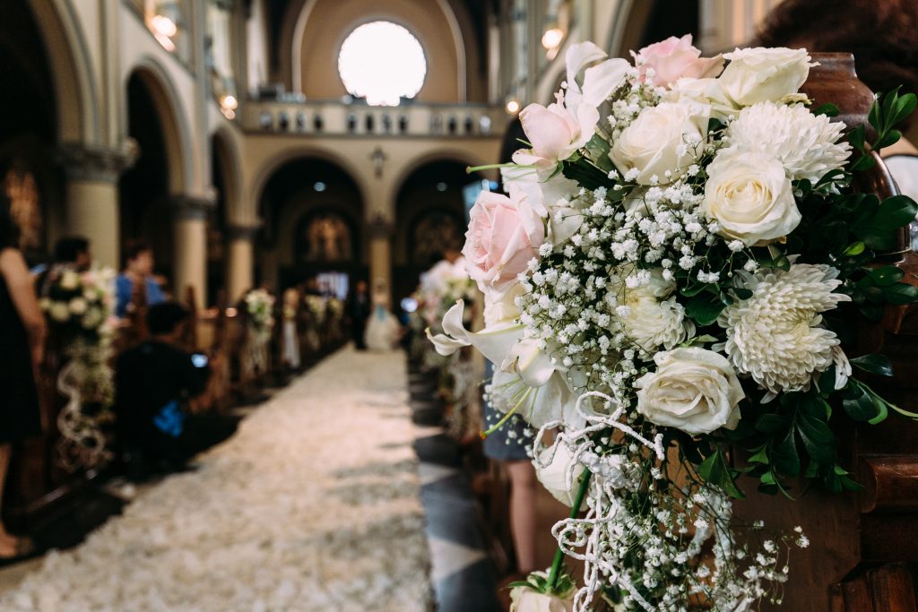 In questa foto una composizione floreale che decora uno dei banchi dei una chiesa per matrimonio. È realizzata con rose bianche e rpsa, nebbiolina e foglie